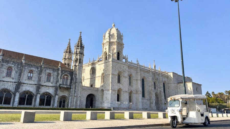 A white tuk-tuk parked in front of Jerónimos Monastery in Belém